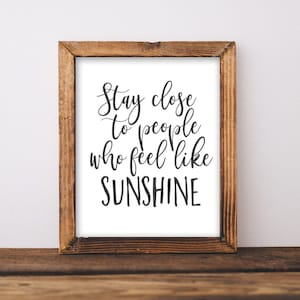 May include: A framed print with a white background and black text that reads "Stay close to people who feel like SUNSHINE". The frame is made of brown wood.