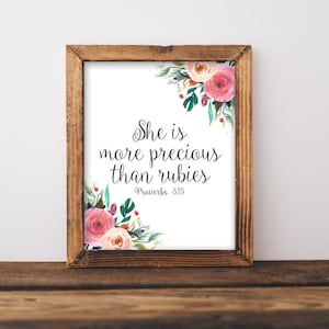 May include: A framed print with a white background and a floral design in the top right corner. The print features the text "She is more precious than rubies" and "Proverbs 3:15".
