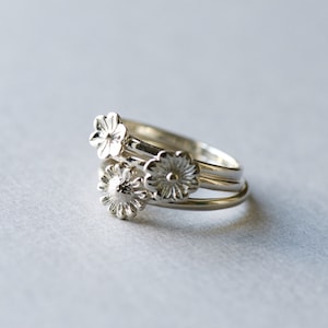 May include: Three silver rings with flower designs. The rings are stacked on top of each other.