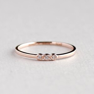 May include: A delicate rose gold band ring with three small round diamonds set in a row.