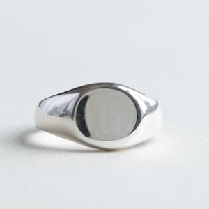 May include: A silver signet ring with a smooth, oval-shaped top.