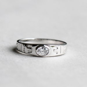 May include: A silver ring with a clear stone set in the centre. The band is engraved with a pattern.