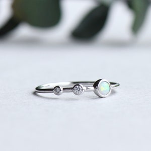 Puede incluir: Un anillo de plata con tres pequeñas piedras redondas, una opala blanca y dos piedras transparentes.