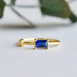 May include: A gold ring with a blue rectangular gemstone. The ring has a simple design and is perfect for everyday wear.