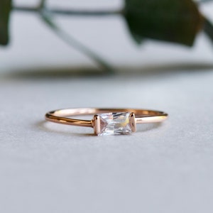 Puede incluir: Un delicado anillo de oro rosa con una piedra rectangular transparente.