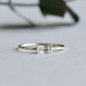 May include: A silver ring with a clear rectangular gemstone.