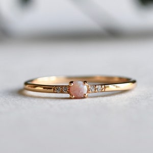May include: A delicate gold ring with a small pink opal gemstone and tiny diamonds set in the band.