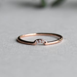 May include: A delicate rose gold band with a row of small diamonds set in a curved arch.