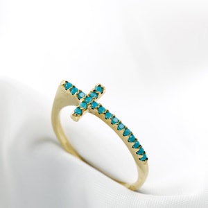 Puede incluir: Un anillo de oro con un diseño de cruz turquesa. La cruz está engastada con pequeñas piedras turquesas.
