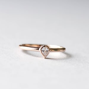 May include: A simple gold band ring with a single pear-shaped clear gemstone.