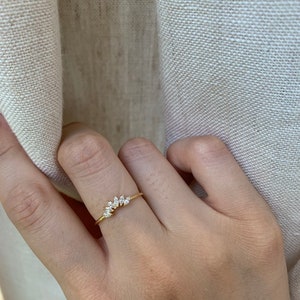 May include: A gold ring with a row of small, clear, marquise-shaped stones set in a curved line.