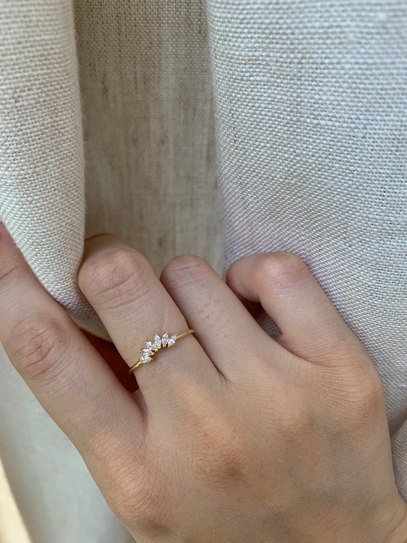 May include: A gold ring with a row of small, clear, marquise-shaped stones set in a curved line.