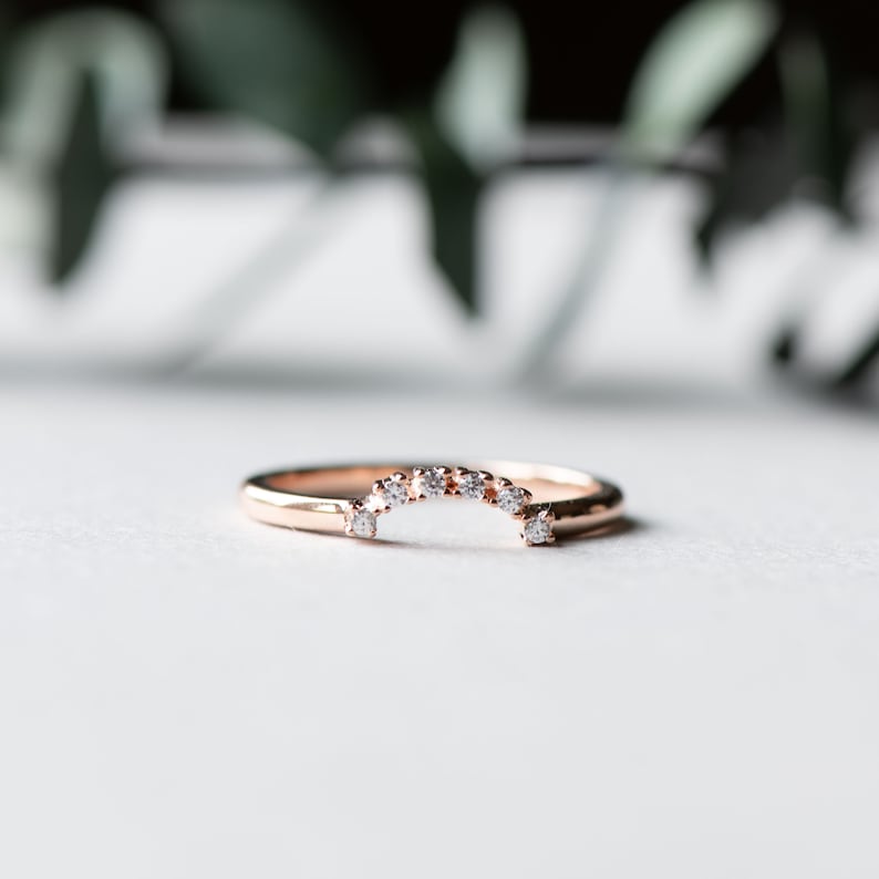 May include: A rose gold wedding band with a row of small diamonds set in a curved arch shape.