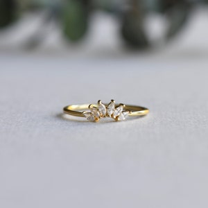 May include: A gold ring with a row of marquise-shaped clear stones set in a curved design.