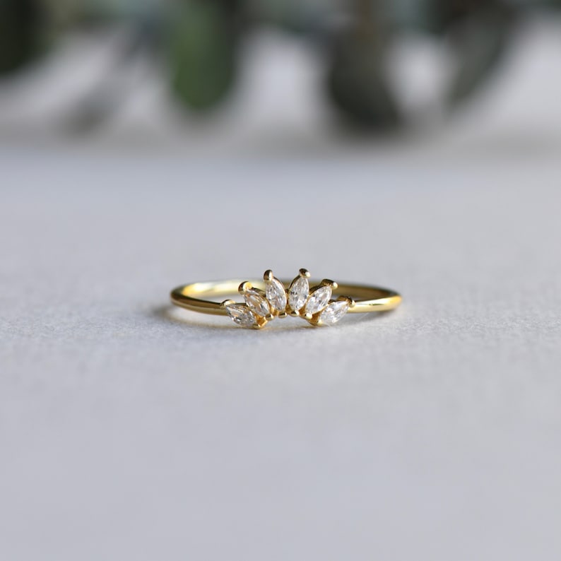 May include: A gold ring with a row of marquise-shaped clear stones set in a curved design.
