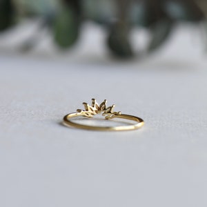 May include: A gold ring with a delicate, leaf-shaped design. The ring is open in the back and has a curved shape.