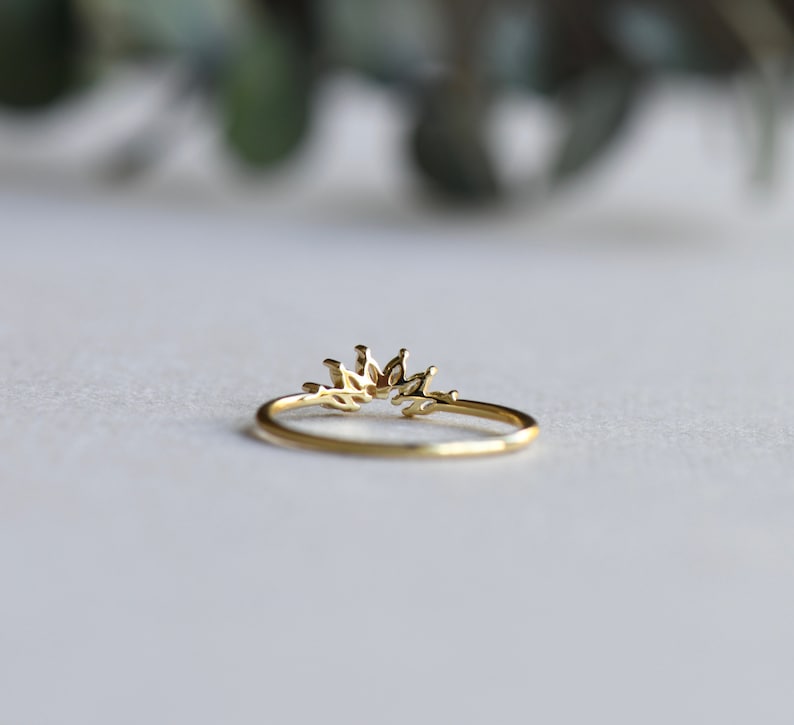 May include: A gold ring with a delicate, leaf-shaped design. The ring is open in the back and has a curved shape.