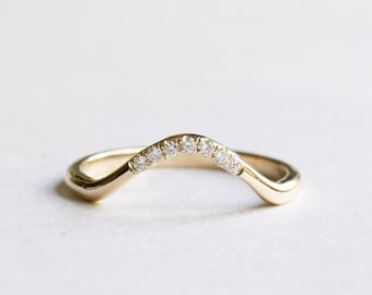 May include: A gold band with a curved, v-shaped design. The band is set with small, round diamonds.
