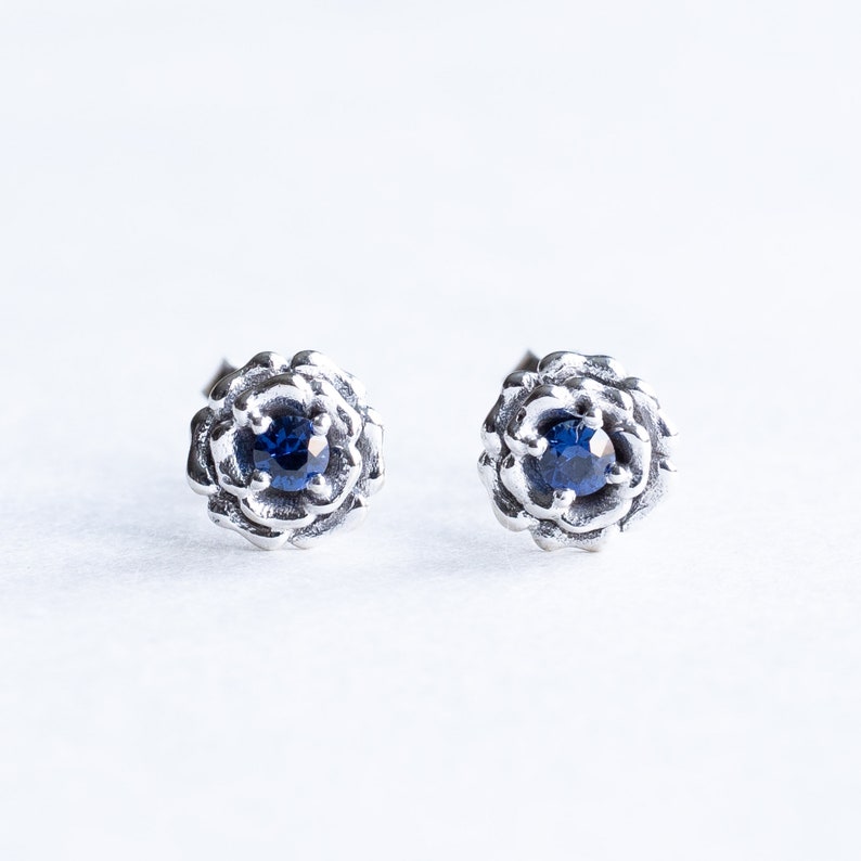 May include: A pair of silver earrings with a blue gemstone set in a flower-shaped design.