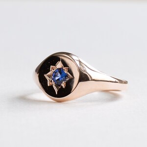 May include: A rose gold signet ring with a blue sapphire set in a star-shaped design.
