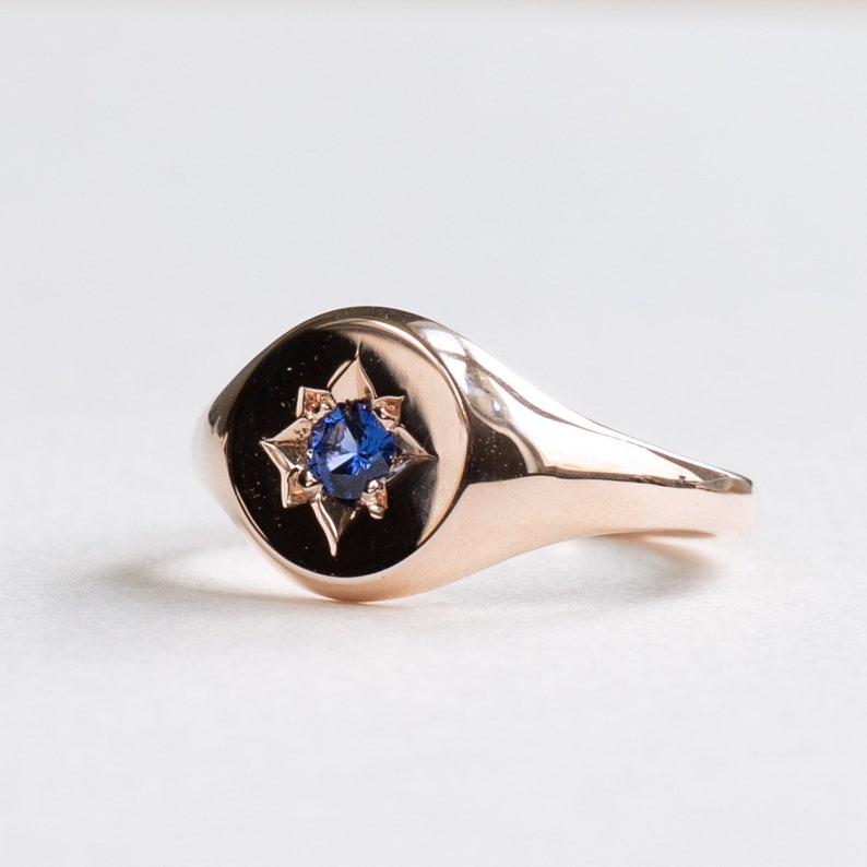 May include: A rose gold signet ring with a blue sapphire set in a star-shaped design.