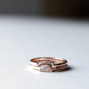 May include: A set of two rose gold rings with a half-moon shaped diamond and a row of smaller diamonds.