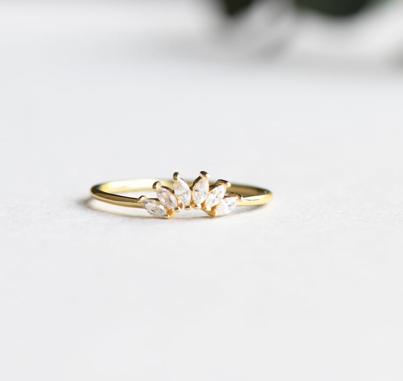 May include: A delicate gold ring with a row of marquise-shaped clear stones set in a curved design.