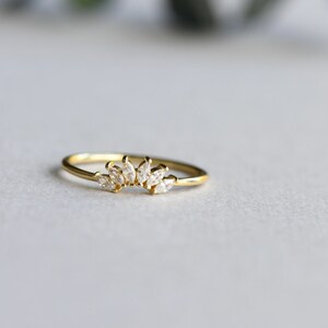 May include: A gold ring with a delicate design of small, clear stones set in a curved line.