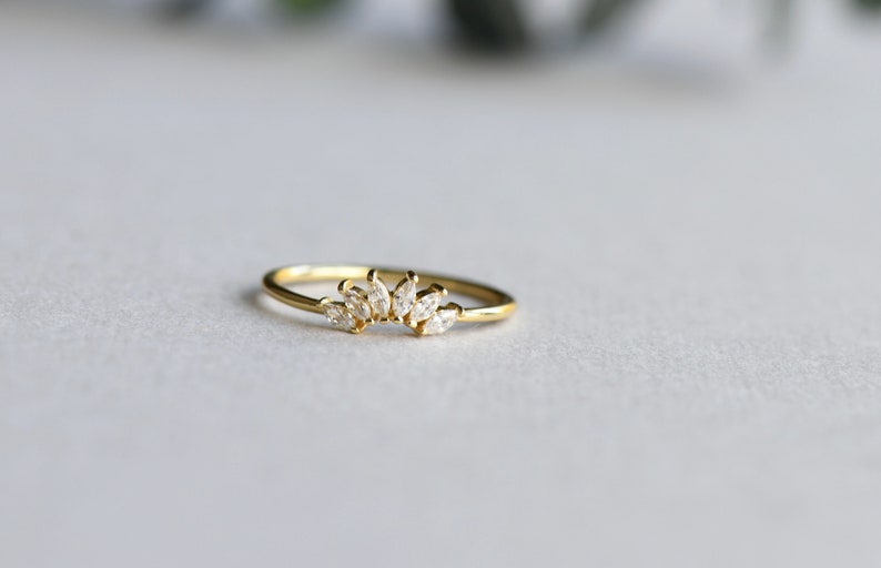 May include: A gold ring with a delicate design of small, clear stones set in a curved line.