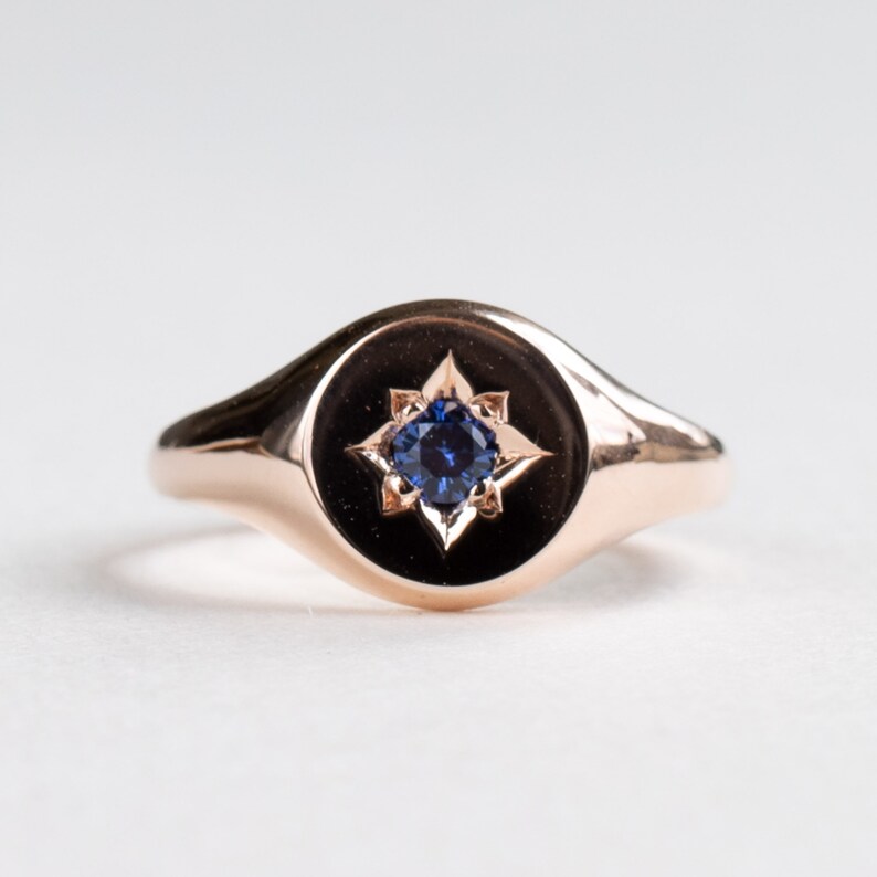 May include: A rose gold signet ring with a blue sapphire set in a star-shaped design.