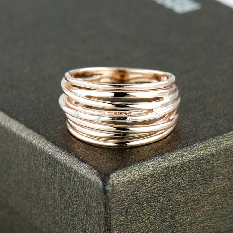 May include: A rose gold ring with multiple bands and small clear stones.