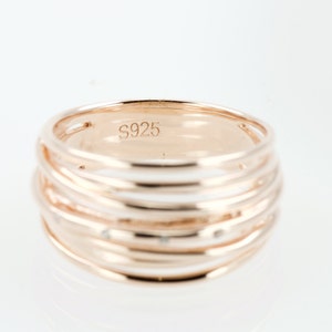 May include: A rose gold ring with multiple bands and small clear stones. The ring is marked with the number "S925" on the inside.