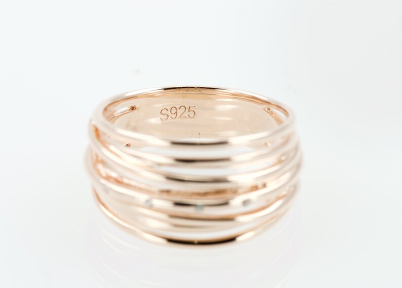 May include: A rose gold ring with multiple bands and small clear stones. The ring is marked with the number "S925" on the inside.