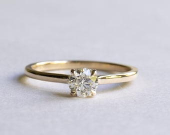 May include: A simple gold band engagement ring with a single round diamond.