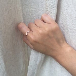 May include: A delicate gold ring with a row of small, clear stones set in a curved shape.