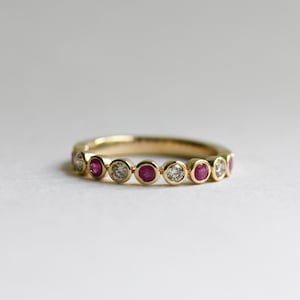 May include: A gold band ring with alternating ruby and diamond stones. The ring is set with bezel-set stones.