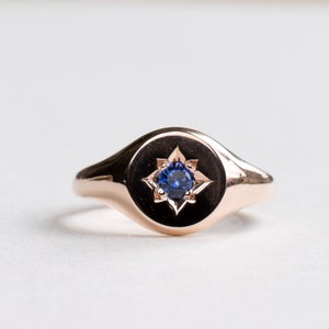 May include: A rose gold signet ring with a blue sapphire gemstone set in a star-shaped design.