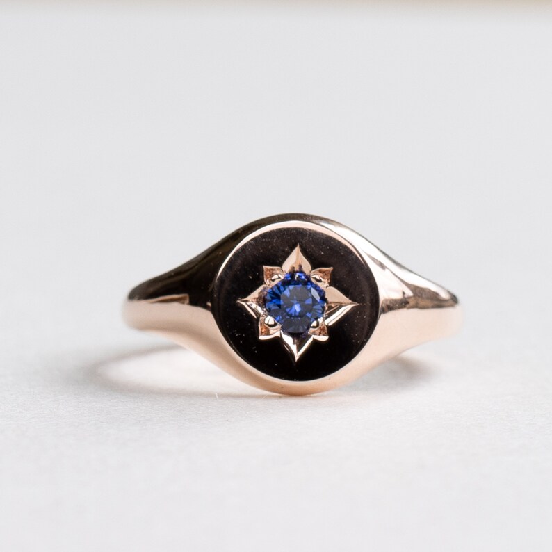 May include: A rose gold signet ring with a blue sapphire gemstone set in a star-shaped design.