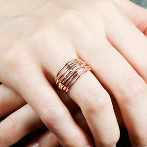 May include: A rose gold ring with multiple bands stacked on top of each other. The ring is worn on a person's finger.