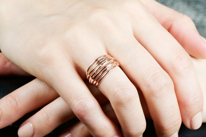 May include: A rose gold ring with multiple bands stacked on top of each other. The ring is worn on a person's finger.