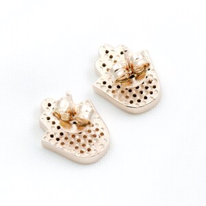 May include: A pair of gold-toned earrings featuring a hamsa hand design. The earrings are made of metal and have a post back fastening.