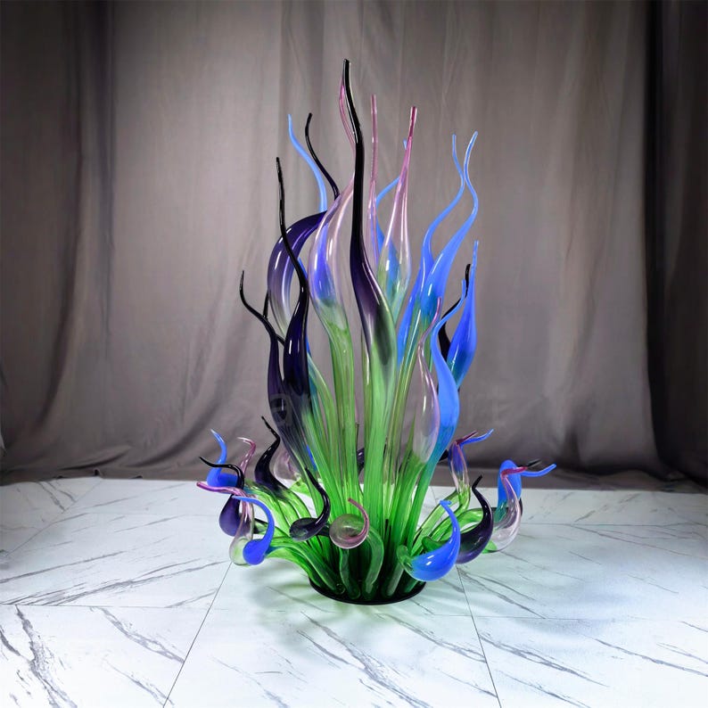 Colorful abstract glass art sculpture with seaweed-inspired shapes, designed for both indoor and outdoor use, shown in a lush green lawn and garden setting as unique yard decor