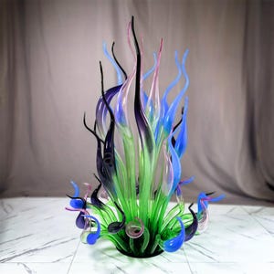 Large hand-blown glass garden sculpture featuring organic flame shapes in green, blue, and purple hues, perfect for elevating outdoor patios, backyard landscapes, and garden focal points