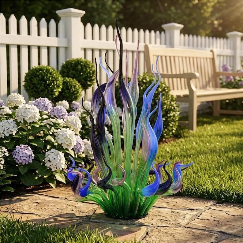 Vibrant hand-blown glass coral sculpture set in a sunlit garden with blooming hydrangeas, showcasing its green base and gradient blue/purple accents as statement outdoor yard art for patios, decks, and garden spaces