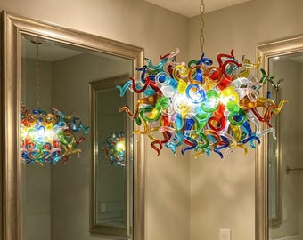 May include: A vibrant glass chandelier with a brass chain, featuring a multitude of swirling shapes in red, blue, green, yellow, and clear glass. The light fixture is reflected in the mirrors on either side of the room.