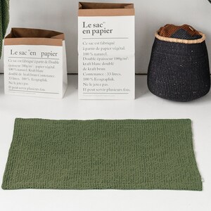 May include: Two brown paper bags with the text "Le sac en papier" on them. The bags are sitting on a black table with a white sink and a green towel. The text on the bags says that they are made from 100% natural paper and have a capacity of 33 litres.