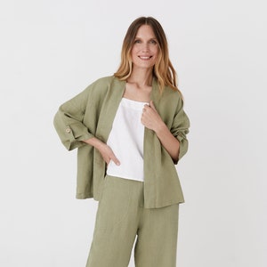 May include: A sage green linen pantsuit with a relaxed fit. The jacket has a shawl collar and long sleeves. The trousers have a wide leg and are cropped.