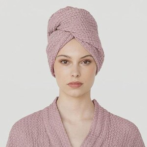 K&ouml;nnte beinhalten: Ein mauvefarbener Waffel-Bademantel und ein passendes Handtuch im Turban-Stil. Der Bademantel hat ein Wickeldesign mit Bindeg&uuml;rtel, Taschen und weiten &Auml;rmeln. Das Handtuch ist um den Kopf gewickelt. Der Stoff hat eine strukturierte Optik.