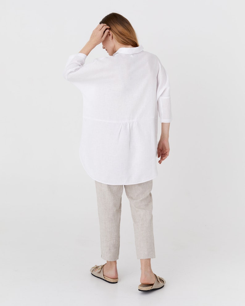 Pode incluir: Uma camisa de linho branca com um caimento relaxado e um comprimento ligeiramente mais longo. A camisa tem colarinho e mangas tr&ecirc;s quartos.
