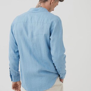 Pu&ograve; includere: Camicia azzurra a maniche lunghe con colletto classico e polsini con bottoni. La camicia &egrave; realizzata in tessuto leggero. Il modello indossa pantaloni beige. La camicia &egrave; tinta unita.